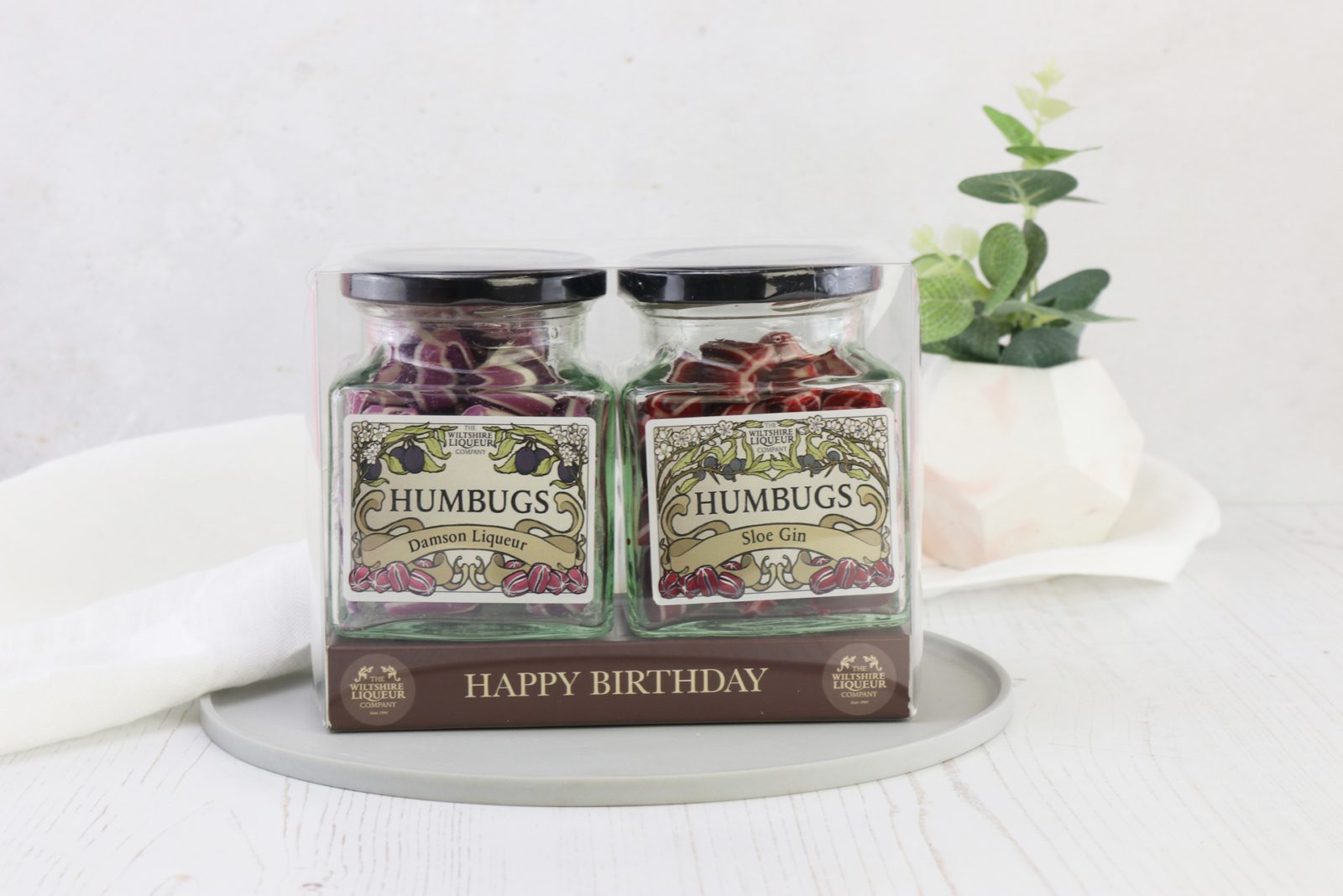 Two jars of Liqueur humbugs with a personalised label that reads: happy birthday. The gift set sits on a white table.
