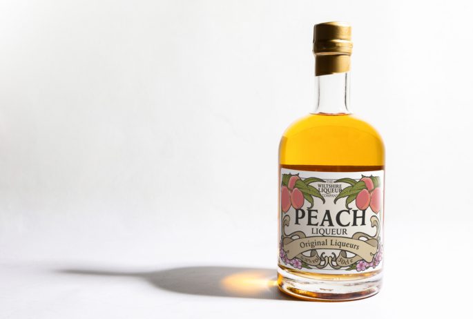 A bottle of Peach Liqueur from the Wiltshire Liqueur Company, on a white background.