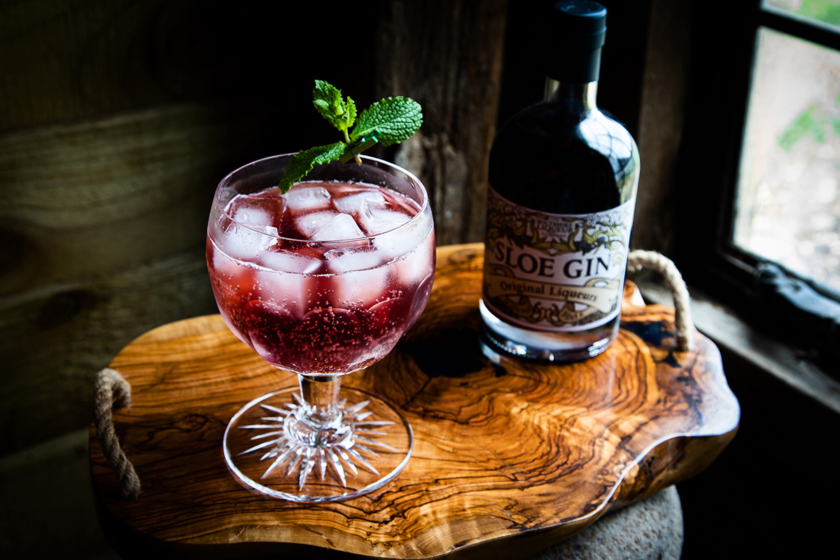 A glass filled with a deep red cocktail made with Sloe Gin.