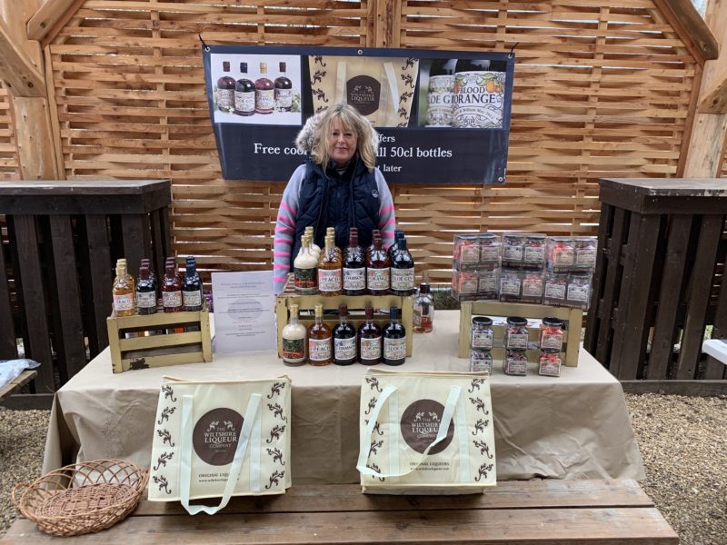 Tiffinie Pride, director and owner of The Wiltshire Liqueur Company stands at the company event stall. Bottles of fruit liqueurs, preserves and branded bags are on display.